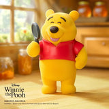 Yellow bear figure in a red shirt holding a gray round accessory in one hand