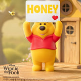 Yellow bear figure holding a “HONEY” sign with a red heart