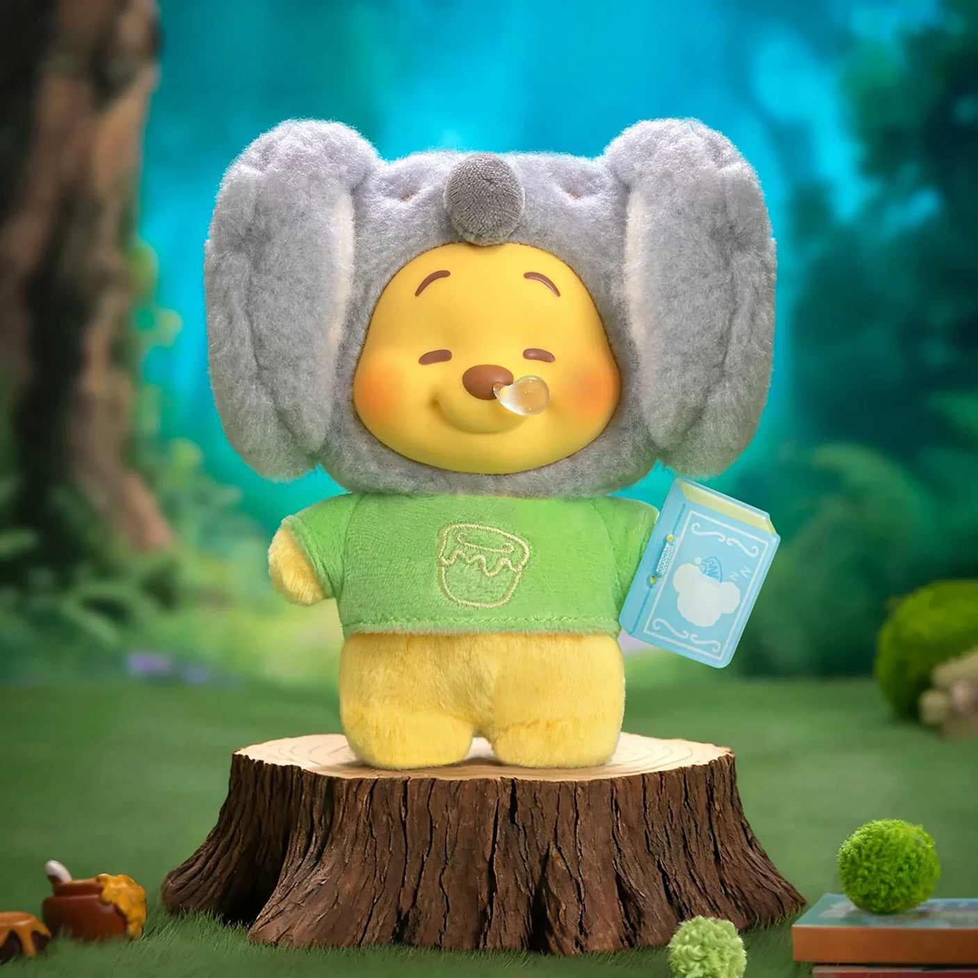 Plush keychain bear in gray ears and green shirt, holding a blue storybook tag.