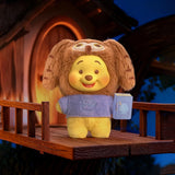 Plush keychain bear in brown fur and purple shirt, holding a blue storybook tag.