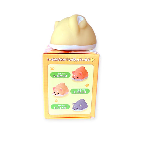 Rear view of yellow Shiba Inu squishy figure perched atop orange blind box showing three collectible Shiba designs on side panel